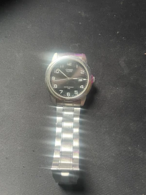 Klassisk silverfärgad Casio klocka går att diskutera pris  - Stilren Casio klocka med svart urtavla och tydliga vita siffror. Armbandet är i blankt silverfärgat metall och klockan har en enkel, klassisk design som passar till det mesta. Perfekt för dig som gillar tidlös stil och vill ha en pålitlig accessoar. 