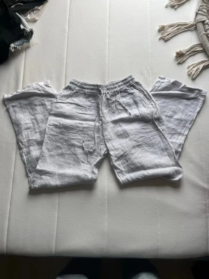 Vita linnebyxor - Säljer ett par vita linnebyxor med avslappnad passform och resår i midjan. Byxorna har raka ben och är tillverkade i ett lätt och luftigt linnetyg, perfekta för varma dagar.