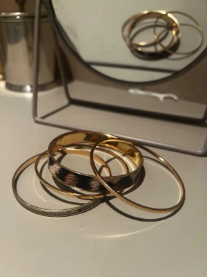 Set med guldiga armband - Säljer ett set med fyra armband i olika stilar. Två är tunna och guldiga, ett är silverfärgat med glittrig yta och ett bredare armband har leopardmönster i svart, beige och brunt. Alla är runda och i metall. Perfekt för dig som gillar att mixa och matcha accessoarer.