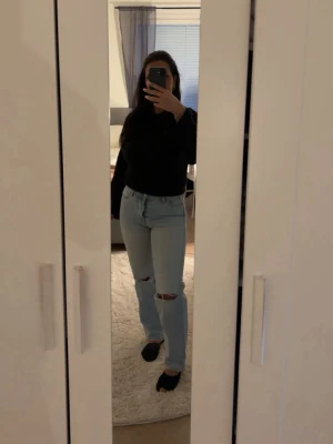 Ljusblå raka jeans med slitningar - Säljer ett par ljusblå jeans med raka ben och slitningar vid knäna. Jeansen har hög midja och klassisk femficksdesign. Perfekta för en avslappnad och trendig look. Materialet är denim i bomull. Märke ej synligt. Från Junkyard