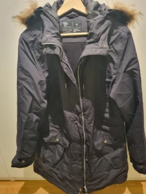 Jacka dam från Neomondo - Svart parkasjacka från Neomondo i storlek XL. Jackan har huva med fuskpäls, dragkedja framtill och praktiska fickor med lock. Perfekt för kalla dagar och har en klassisk, lite längre modell.