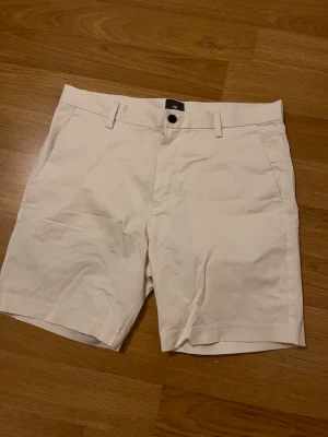 Beiga shorts från H&M Regular Fit - Säljer ett par stilrena beiga shorts från H&M med regular fit. De har klassisk design med knapp och dragkedja framtill, hällor för bälte och två sidofickor. Perfekta för varma dagar och enkel att matcha med olika outfits.