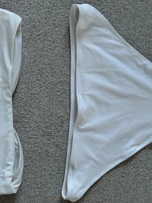 Vit bikini stl 38/M Ny - Bikiniöverdel i bandeaumodell med vadderade kupor, korsas ovanför byst och knyts sedan i nacken. Bikiniunderdel i trosa/bikini briefs modell. Ny. H&M. Vit. Stl 38/M. Rök o djurfritt hem.