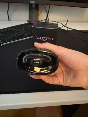 Valentino Uomo Born In Roma parfym 100ml - Säljer en Valentino Uomo Born In Roma parfym, 100ml. Flaskan är svart med nitar och har en lyxig, edgy design. Förpackningen är svart med rosa text och matchar flaskans stilrena look. Perfekt för dig som gillar exklusiva dofter och snygg design.