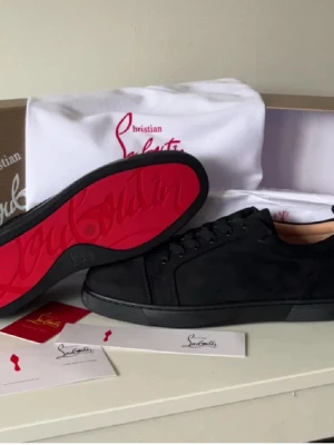 Svarta sneakers från Christian Louboutin - Stilrena svarta sneakers i mocka från Christian Louboutin med klassisk röd sula och svarta skosnören. Låg modell med diskreta metalldetaljer och signatur på innersulan. Perfekta för dig som vill ha en lyxig och trendig look.