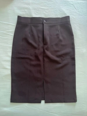 Svart pennkjol med slits - Klassisk svart pennkjol med slits framtill och enkel knappstängning i midjan. Kjolen har en rak och elegant form som passar till många olika stilar. Tillverkad i ett mjukt material som känns bekvämt mot huden.