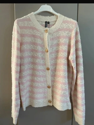 Randig kofta från Soulmate, S ny med prislappen  - Mysig kofta från Soulmate i storlek S med ljusrosa och vita ränder. Koftan har långa ärmar, rund halsringning och dekorativa guldknappar framtill. Materialet är mjukt och strukturerat, perfekt för en chill look.