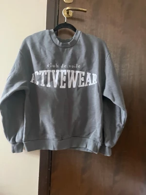 Grå sweatshirt Gina Tricot - Säljer en grå sweatshirt från Gina Tricot med stor vit text 'ACTIVEWEAR' framtill. Tröjan har rund halsringning, ribbade muddar vid ärmslut och nederkant samt en avslappnad passform. Säljer för att den inte används. Storlek XXS.