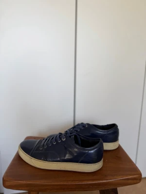 Lanvin - Snygga mörkblå sneakers i glansigt läder med vita sulor och matchande mörkblå skosnören. Klassisk låg modell som passar till det mesta och ger en clean look. Perfekta för dig som gillar stilrena och tidlösa skor.