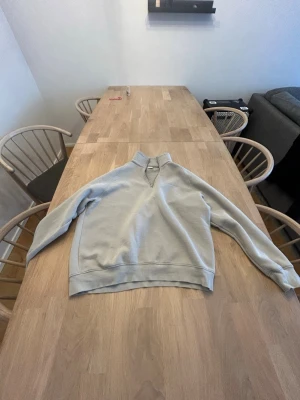 NN07 halvzip hoodie - En stilren beige/hjusgrön hoodie med halvzip och hög krage. Tillverkad i mjukt sweatshirtmaterial och har ribbade muddar vid ärmslut och nederkant. Perfekt för en avslappnad look och enkel att matcha med jeans eller mjukisbyxor. Den är s men passar m