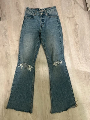 Blå slitna bootcut jeans med hål - Säljer ett par blå bootcut jeans med hål vid knäna. Pris kan alltid diskuteras 💕