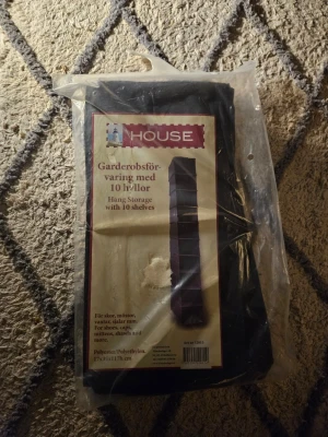 Garderobsförvaring med 10 hyllor nytt I förpackningen  - Praktisk garderobsförvaring från House med 10 hyllor, perfekt för skor, mössor, vantar och andra småprylar. Tillverkad i polyester och polyetylen, svart färg. Mått: 17x35x117 cm. Enkel att hänga upp i garderoben för smidig organisering.