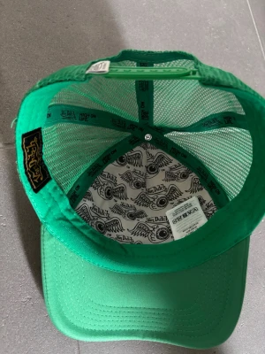 Grön Von Dutch truckerkeps - Cool grön truckerkeps från Von Dutch med vit broderad logga på framsidan. Kepsen har mesh-paneler på sidorna och baksidan för extra ventilation och en böjd skärm. Materialet är polyester och bomull, perfekt för en avslappnad streetstyle.