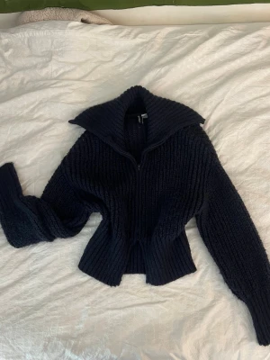 Mörkblå stickad tröja med krage - Säljer en chunky mörkblå stickad tröja med bred krage och dragkedja framtill. Tröjan har ribbstickad struktur, långa ärmar och en något croppad passform. Perfekt för dig som gillar en avslappnad men ändå stilren look.