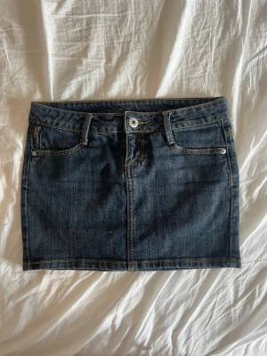 Tally weijl jeanskjol - Snygg mörkblå jeanskjol i klassisk modell, bälteshällor och kontrastsömmar. Kjolen är  i väldigt fint skick förutom en liten ”fläck” framtill, se bild 4. Man får kolla ganska noga för att se ”fläcken” så inget som riktigt märks skulle jag säga. Midjemåttet rakt över : 38cm, längden av kjolen : 35cm. Kjolen är i storlek 36/S. Passar till det mesta och är enkel att matcha.