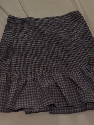 Lila rutig kortkjol med volang - Supersöt lila och vit rutig kortkjol med volangkant nedtill. Kjolen har smock i midjan för en bekväm passform och är perfekt för dig som gillar en avslappnad men ändå trendig stil. 