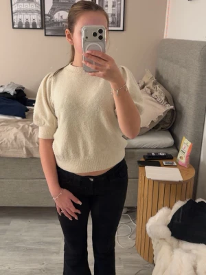 Krämvit stickad topp med puffärm - Säljer en krämvit stickad topp med korta puffärmar och ribbad kant vid hals och nederkant. Materialet är mjukt och bekvämt.  Har aldrig kommit till användning så den är i ett väldigt bra skick.