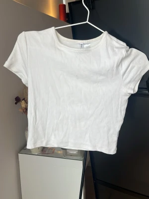 Vit ribbad croppad topp från H&M - Säljer en enkel och stilren vit croppad topp från H&M. Toppen är ribbad och har korta ärmar samt rund halsringning. Perfekt att matcha med höga jeans eller kjol för en clean look.