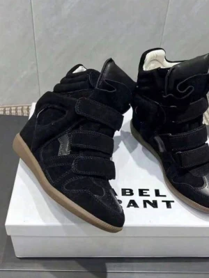 Isabel Marant svarta höga sneakers - Svarta höga sneakers från Isabel Marant med flera kardborreband och beige sula. Skorna är tillverkade i mocka och läder, har vadderad plös och krage för extra komfort samt en unik design som sticker ut. Perfekta för dig som vill ha en statement sneaker.