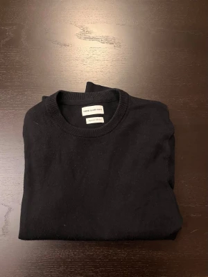 Marinblå stickad tröja These Glory Days - En stilren marinblå stickad tröja från These Glory Days med rund halsringning och ribbade muddar vid ärmslut och nederkant. Tröjan är enkel och klassisk i modellen.