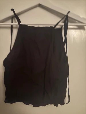 Svart crop top med knytband H&M - Säljer en svart crop top från H&M med tunna axelband som knyts upptill. Toppen har en lös passform och är gjord i ett lätt, skrynkligt tyg som ger en avslappnad vibe. Perfekt till sommaren eller festivalen!
