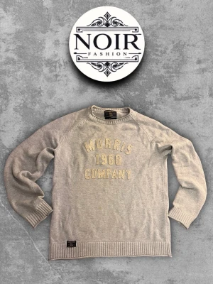 Grå tröja från Morris Company - Snygg grå tröja från Morris Company med broderad text 'Morris 1968 Company' på bröstet. Tröjan har rund halsringning, långa ärmar och ribbade muddar vid ärmslut och nederkant. Perfekt för en stilren och avslappnad look.