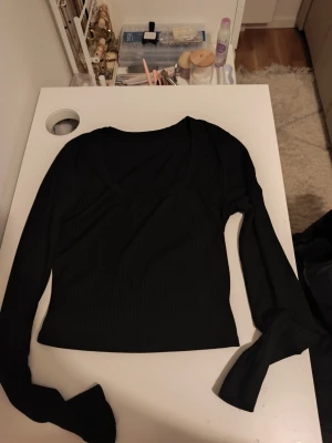 Svart ribbad långärmad topp - Snygg svart ribbad topp med lång ärm och v-ringning. Modellen är croppad och har en smickrande passform som passar perfekt till jeans eller kjol. Enkel men stilren design som är lätt att matcha.