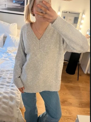Ljusgrå stickad tröja med v-ringning - Mysig ljusgrå stickad tröja med djup v-ringning och avslappnad passform. Super mjukt material, i mycket bra skick! 