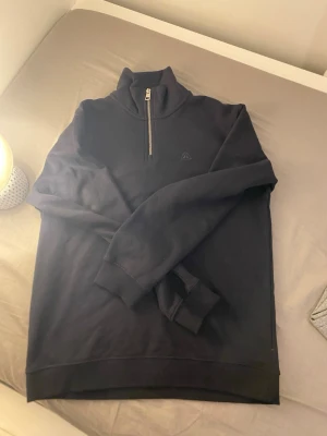 Svart half-zip hoodie från Asket - Säljer en svart hoodie från Asket med half-zip dragkedja och hög krage. Tröjan har långa ärmar, ribbade muddar och är tillverkad i mjukt bomullsmaterial. Minimalistisk design med diskret logga på bröstet. Perfekt för en clean och stilren look.