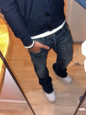Mörkblåa bootcut jeans från Diesel - Säljer ett par mörkblåa bootcut jeans från Diesel med snygga slitningar och tvättade detaljer. Jeansen har klassisk femficksdesign, låg midja och är tillverkade i mjuk denim. Perfekta för en avslappnad och trendig look.