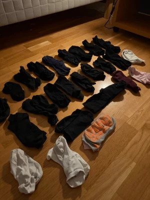 Stort paket med blandade strumpor - Säljer ett paket med flera par strumpor i olika färger och modeller. Mest svarta, men även vita, blå, lila, rosa och ett par med orange text. Perfekt för dig som vill fylla på strumplådan snabbt. De flesta är i bomull och syntetblandning.