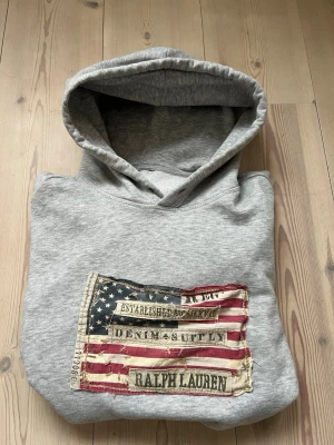 Ralph lauren hoodie. OBS Necktaggen är borta. - Snygg grå hoodie från Ralph lauren/denim and supply.  Perfekt för en stilren casual look🤩. Tveka inte att ställa frågor🤝necktaggen är borta❌Storleken står inte men skulle säga att den passar M