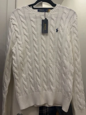 Polo Ralph Lauren kabelstickad tröja – vit - Klassisk vit cable knit från Polo Ralph Lauren med mörkblå broderad logga på bröstet. Tidlös modell som passar både uppklätt och casual. Perfekt till jeans, chinos eller under jacka.  Helt ny. Stilren och alltid rätt. 