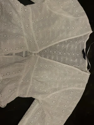 Vit broderad blus från ZARA - Söt vit blus från ZARA med broderade blommor och hålmönster. Blusen har omlottmodell och långa ärmar med lätt puff. Tillverkad i ett tunt, luftigt tyg som känns perfekt för sommaren. Romantisk och trendig look som passar till jeans eller kjol. 