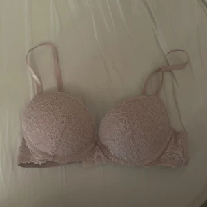 Ljusrosa spets-bh med push up - Söt ljusrosa bh med push up och spetsdetaljer över hela framsidan. Justerbara axelband och hakknäppning bak. 