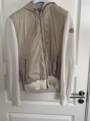 Beige hoodiejacka med stickade ärmar - Snygg beige hoodiejacka med stickade vita ärmar och huva. Jackan har dragkedja framtill, två fickor med dragkedja och ribbade muddar. Perfekt för lager-på-lager och chill stil. Askön cardigan från moncler, inköpt från kicksnstuff förra året för 6999kr. Använd varsamt men har lite slitage nedanför, söker bud så skriv gärna i dm!