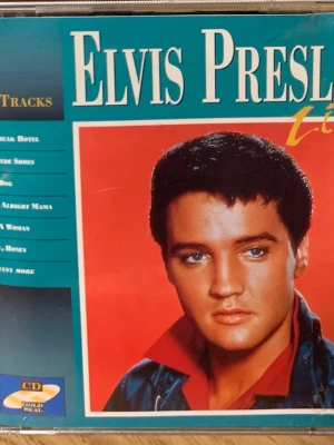 Elvis Presley Live CD - CD med Elvis Presley Live, innehåller klassiska låtar som Heartbreak Hotel, Blue Suede Shoes och Hound Dog. Omslaget är blått med en bild på Elvis och låtlista på baksidan. Perfekt för dig som gillar rock'n'roll och samlar på musik.