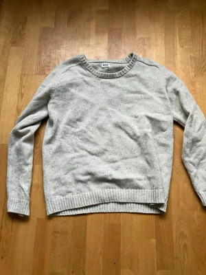 Beige stickad tröja från Weekday - Säljer en beige stickad tröja från Weekday med diskreta färgstänk i blått och svart. Tröjan har rund halsringning, långa ärmar och ribbade muddar vid ärmslut och nederkant. Perfekt för dig som gillar enkel och stilren design.