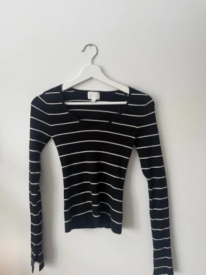 Svartvit randig ribbad topp H&M - Svart långärmad topp från H&M med vita ränder. Toppen är ribbad och har en v-ringad halsringning. Sitter tight och har slits vid ärmens slut. Storlek S. Använt cirka 2-3 gånger.
