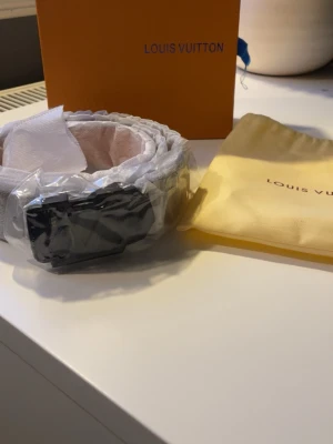 Svart Louis Vuitton bälte med LV-spänne - Snyggt svart bälte från Louis Vuitton med det ikoniska LV-spännet i metall. Bältet har en stilren design och kommer med originalförpackning och dustbag. Perfekt accessoar för att lyfta vilken outfit som helst. Helt oanvänt då det inte passade och returdatumet passerade.