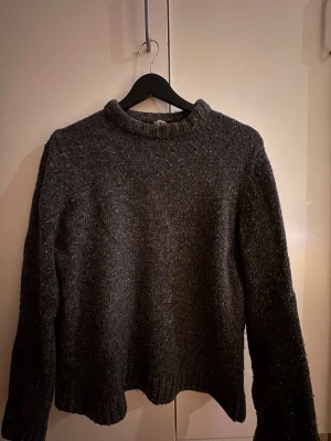 Arket Mörkgrå stickad tröja  - ArketMysig mörkgrå stickad tröja med rund hals och långa ärmar. Tröjan har en enkel, rak passform och ribbstickade muddar vid ärmslut och nederkant. Perfekt för kalla dagar och lätt att matcha med olika outfits.