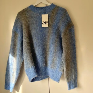 Blå och grå tröja  - Säljer en mysig blå och grå tröja från Zara helt oanvänd. Tröjan har en fluffig textur och långa ärmar, perfekt för kyliga dagar. Den har en rund halsringning och en avslappnad passform. Föör snygg! 