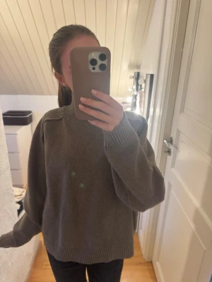 Brun stickad tröja med hög krage - Mysig brun stickad tröja med hög ribbad krage och avslappnad passform. Tröjan har långa ärmar och ribbade muddar vid ärmslut och nederkant. 