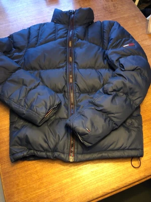 Dunjacka Tommy Hilfiger stl S. - Stilren. Ganska mörkt blå. Dragsko i midjan. Modellen har egentligen en löstagbar luva men den hittar jag givetvis inte. Mkt sparsamt använd. Inga revor eller fläckar.  #tommyhilfiger, #dun, #down, #unisex