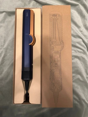 Dyson Airstrait hårstyler blå/koppar - Säljer en oanvänd helt ny Dyson Airstrait hårstyler i snygg blå och kopparfärg. Den har en modern, avlång form och levereras i originalförpackning med tillhörande sladd och adapter. Perfekt för att styla håret med avancerad teknik och elegant design. 