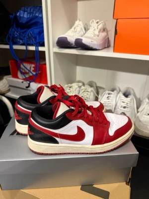 Air Jordan 1 Low Chicago - Säljer ett par Air Jordan 1 Low Chicago med klassisk färgkombination i rött, vitt och svart. Skorna har röd Swoosh, röda snören och svart häl med Air Jordan-logga broderad bak. Ovandelen är i läder och sulan är vit med röd yttersula.