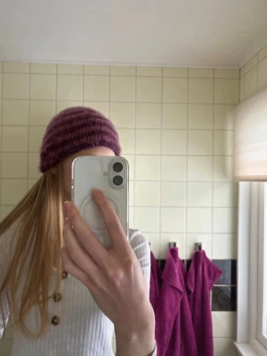Lila-randig stickad mohairmössa - Mysig stickad mössa i fluffigt mohairmaterial med breda ränder i två olika lila nyanser. Mössan har en klassisk form och är perfekt för att hålla värmen under kalla dagar. Passar dig som gillar en trendig och personlig stil. Ps är egenvirkad💜passar mig bra som har en huvudomkrets på ca 57cm