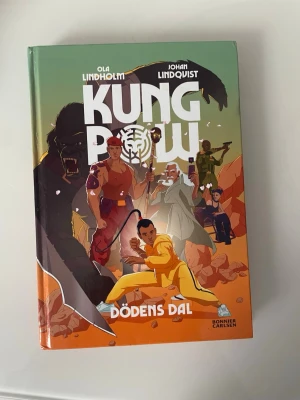 Kung Pow: Dödens dal - En färgstarke och actionfylld bok med titeln 'Kung Pow: Dödens dal' av Ola Lindholm och Johan Lindqvist. Omslaget visar tecknade karaktärer i kampsportspose, gorillor och äventyr i djungelmiljö. Perfekt för dig som gillar spänning, humor och äventyr.