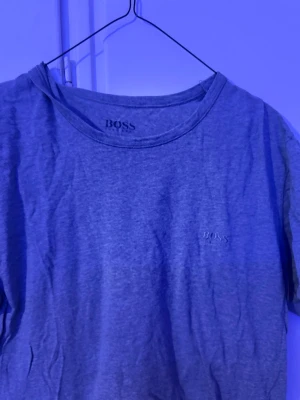 Grå t-shirt från BOSS - En stilren grå t-shirt från BOSS med diskret logga broderad på bröstet. Klassisk rund halsringning och korta ärmar. Perfekt basplagg för en enkel och clean look.