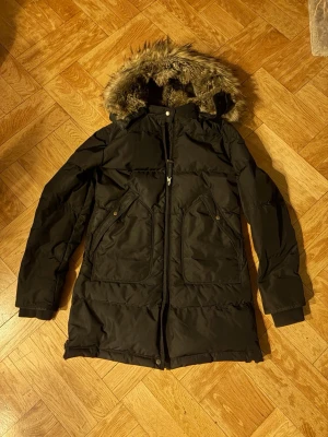 PARAJUMPERSLONG BEAR GIRL JACKET JUNIOR STL MEDIUM - Färg: svart  Storlek: Young Medium. Observera- M för barn/ungdom Skick: Fint! Använd två säsongen av min dotter, men är väl omhändertagen och i fint skick! Jackan är av den tidigare modellen som har den härliga pälsen i luvan, vilket saknas på årets modell.   Kids' Long Bear Hooded Parka från Parajumpers är en varm dunparkas för barn, gjord i återvunnen nylon och är en tidlös klassiker från Masterpiece-kollektionen. Läs mer på återförsäljarens hemsida för mer info.  